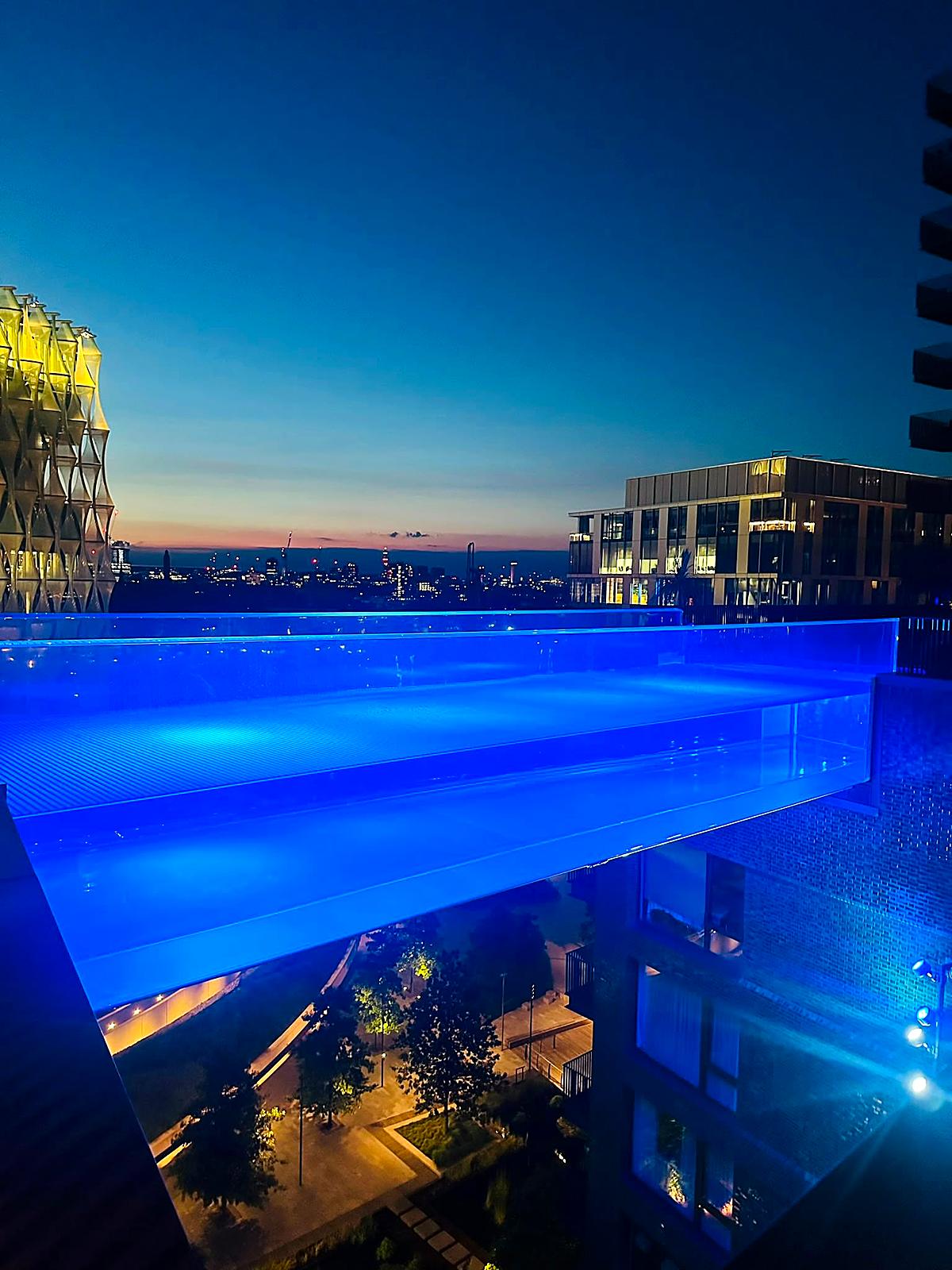 The Sky Pool at Embassy Gardens lit blue at dusk, with the US Embassy beyond